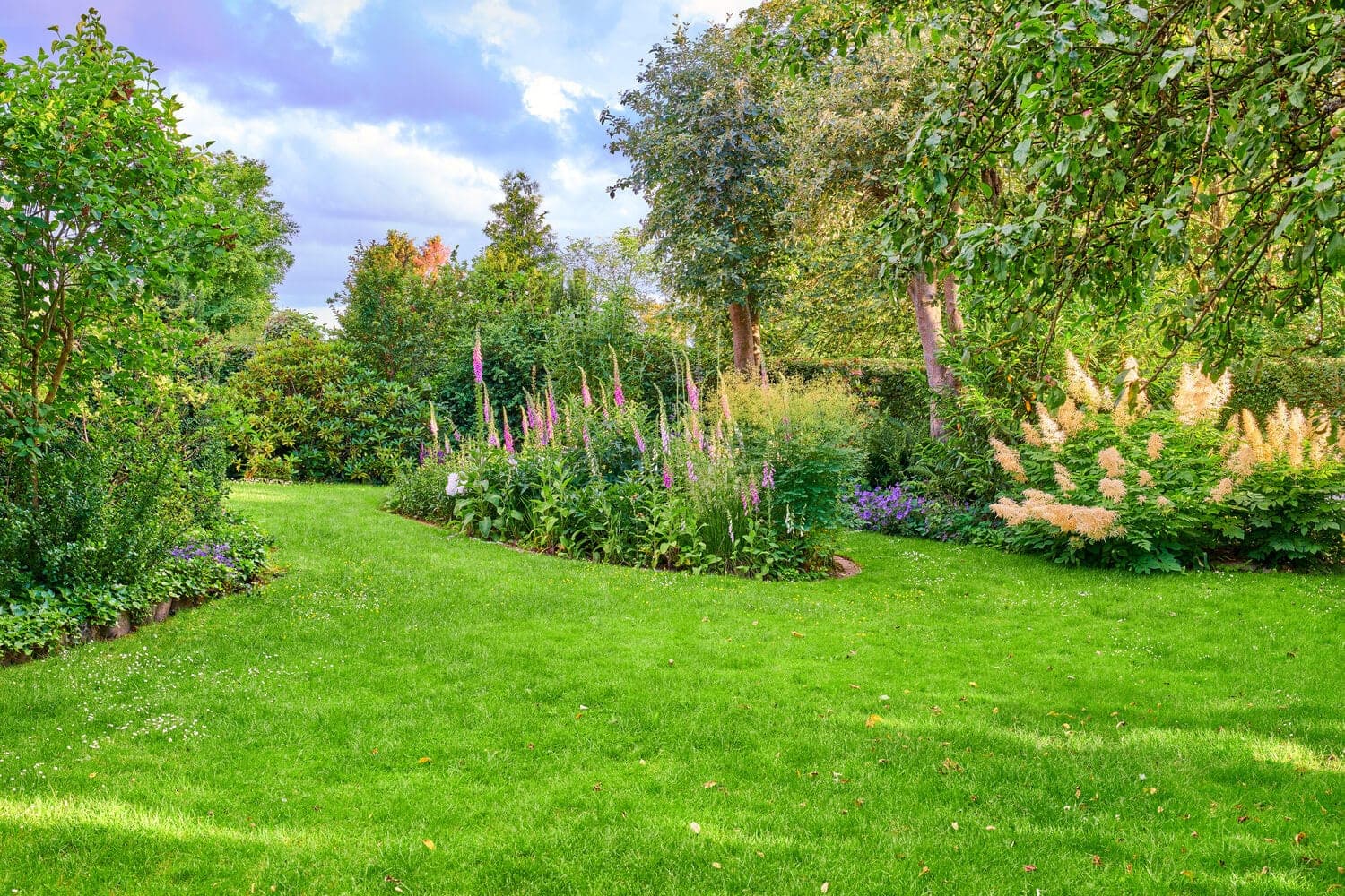 Lawn bordered by trees, shrubs and flowering garden beds