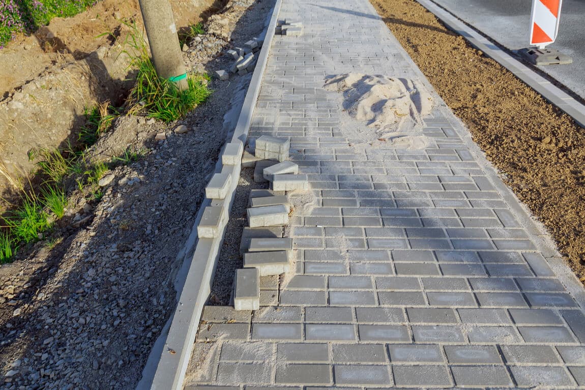 Partially installed paving stones beside an excavated strip of soil