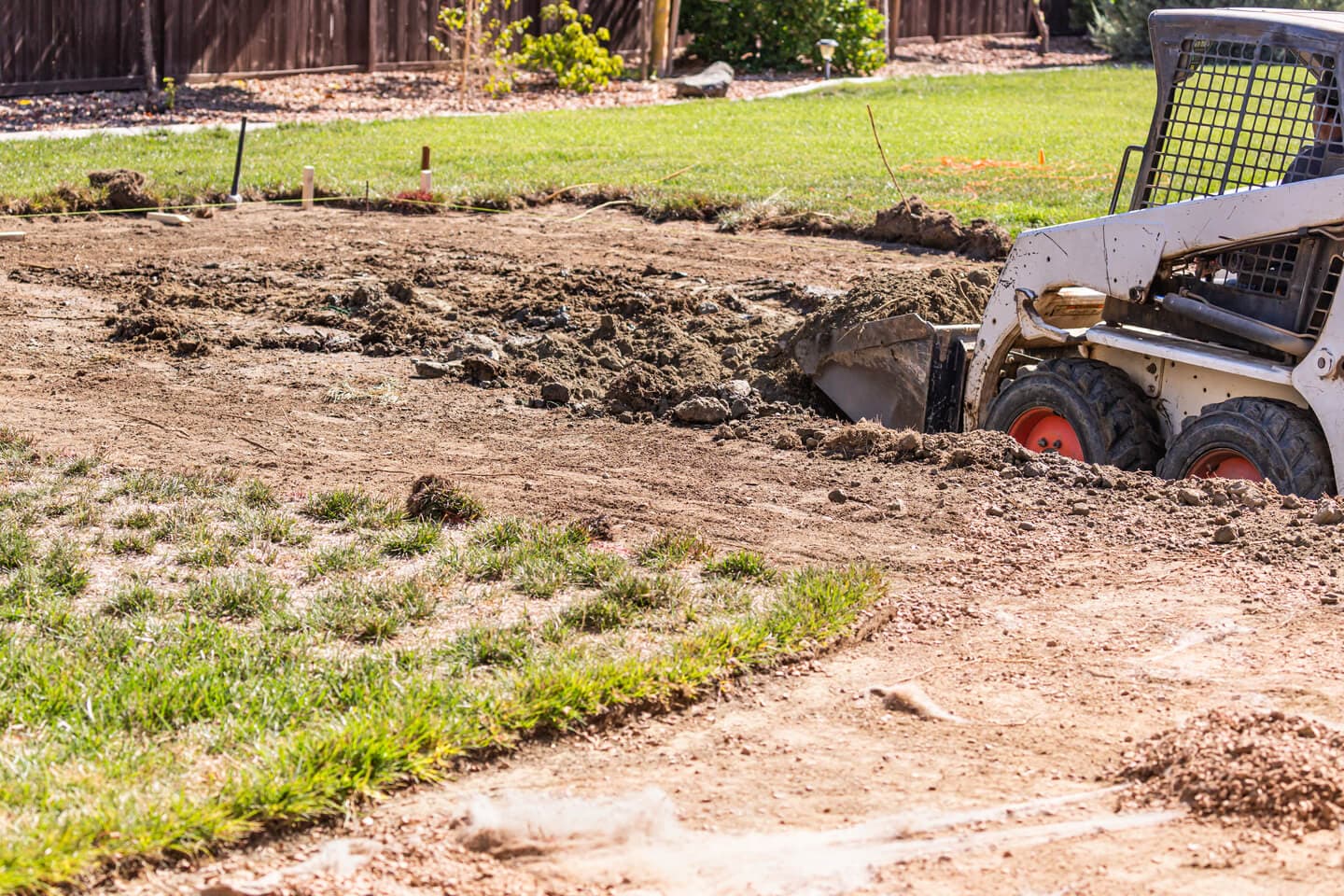 Compact loader digging soil in a residential yard