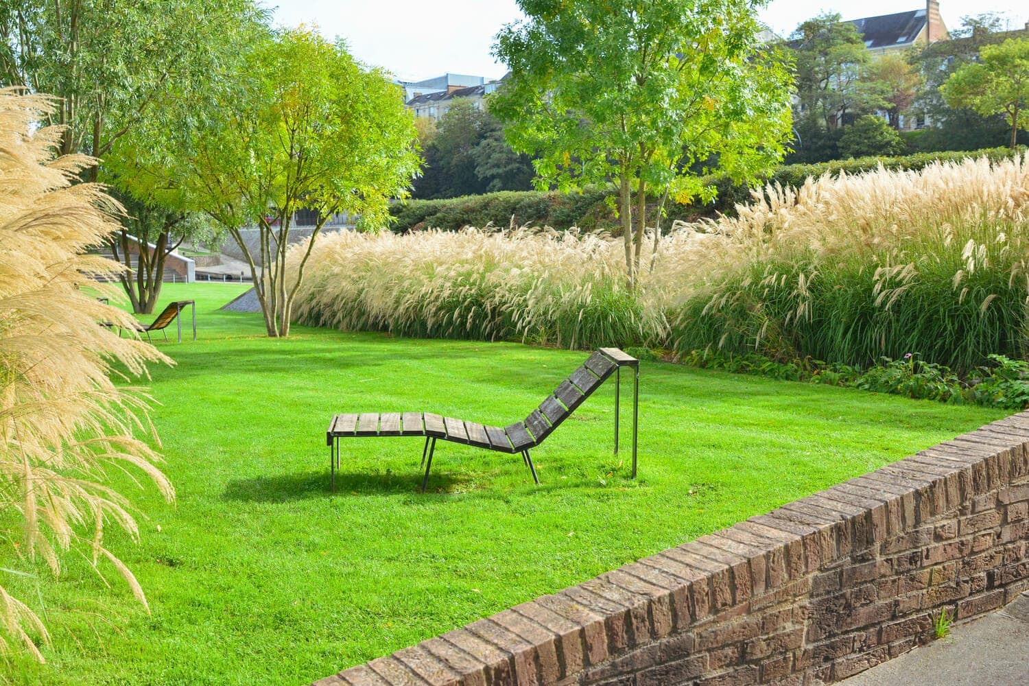 Lawn and lounge chair bordered by ornamental grasses and trees
